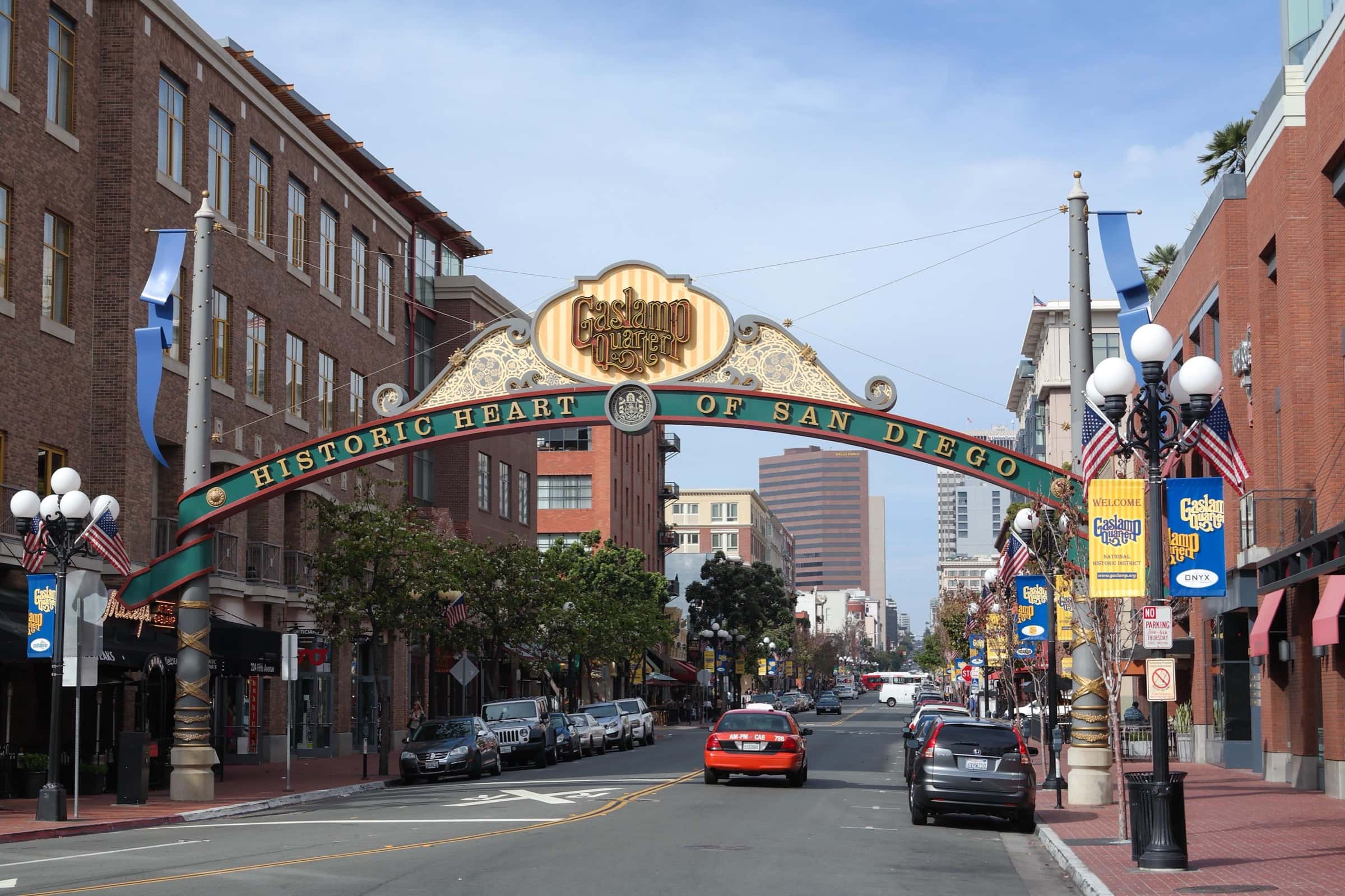 The Gaslamp Quarter arch reading Historic Heart of San Diego over Fifth Avenue, with red-brick buildings, globe streetlamps and downtown towers beyond