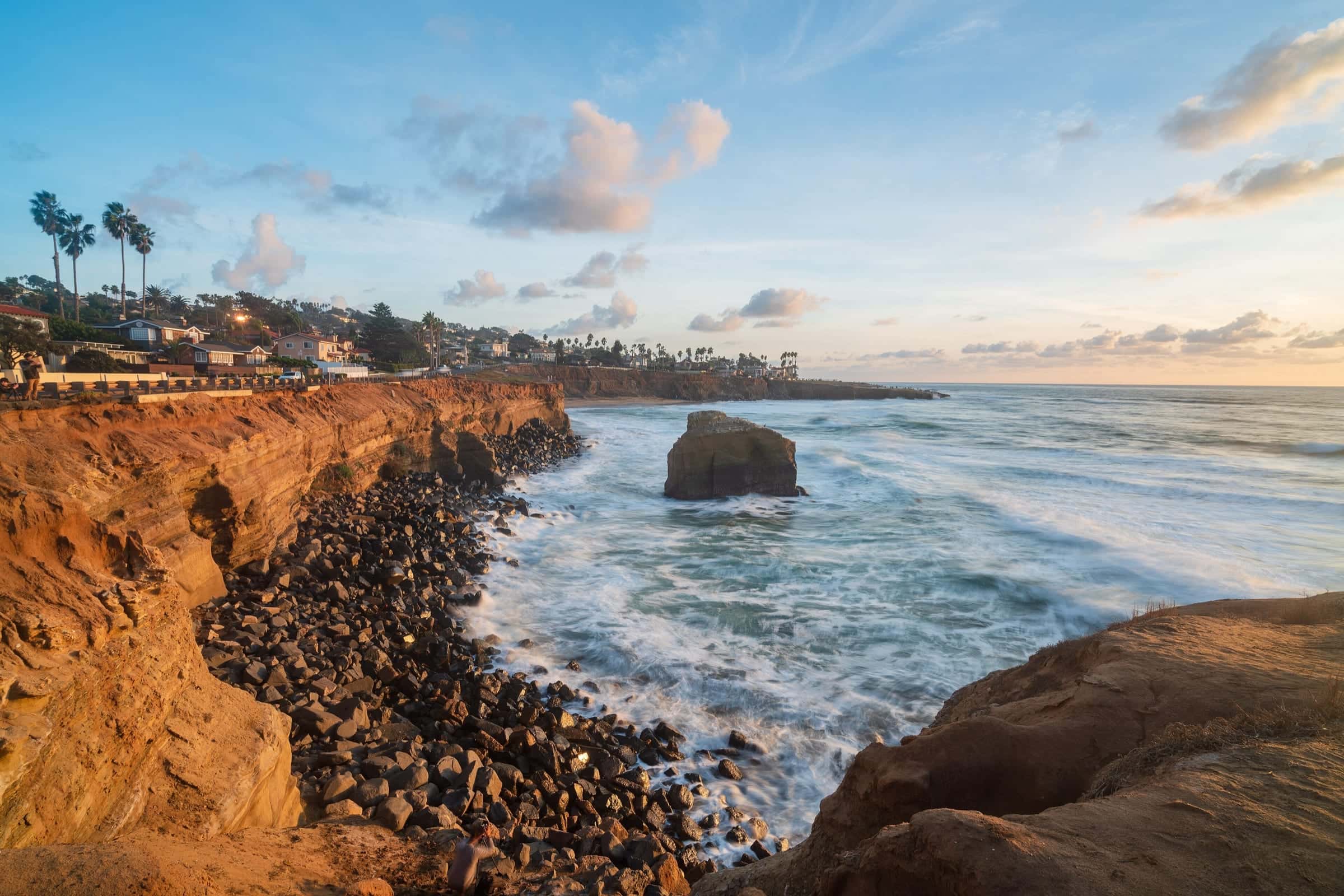 Sunset Cliffs in Point Loma at golden hour, with sandstone bluffs, a sea stack offshore, and homes along the cliff top