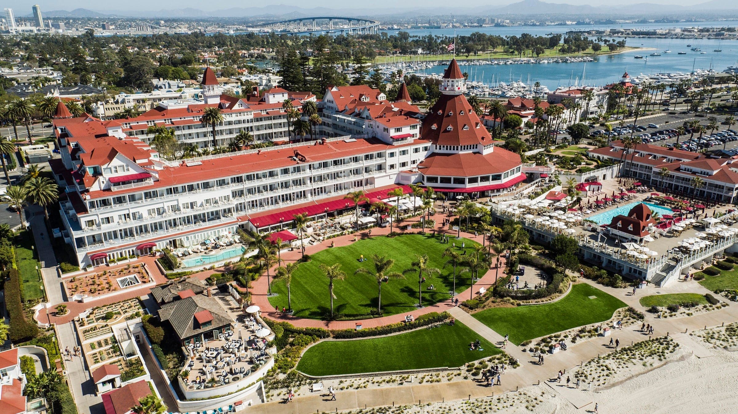 Aerial view of the Hotel del Coronado and its oceanfront lawn, with Glorietta Bay, the Coronado Bridge, and downtown San Diego in the distance