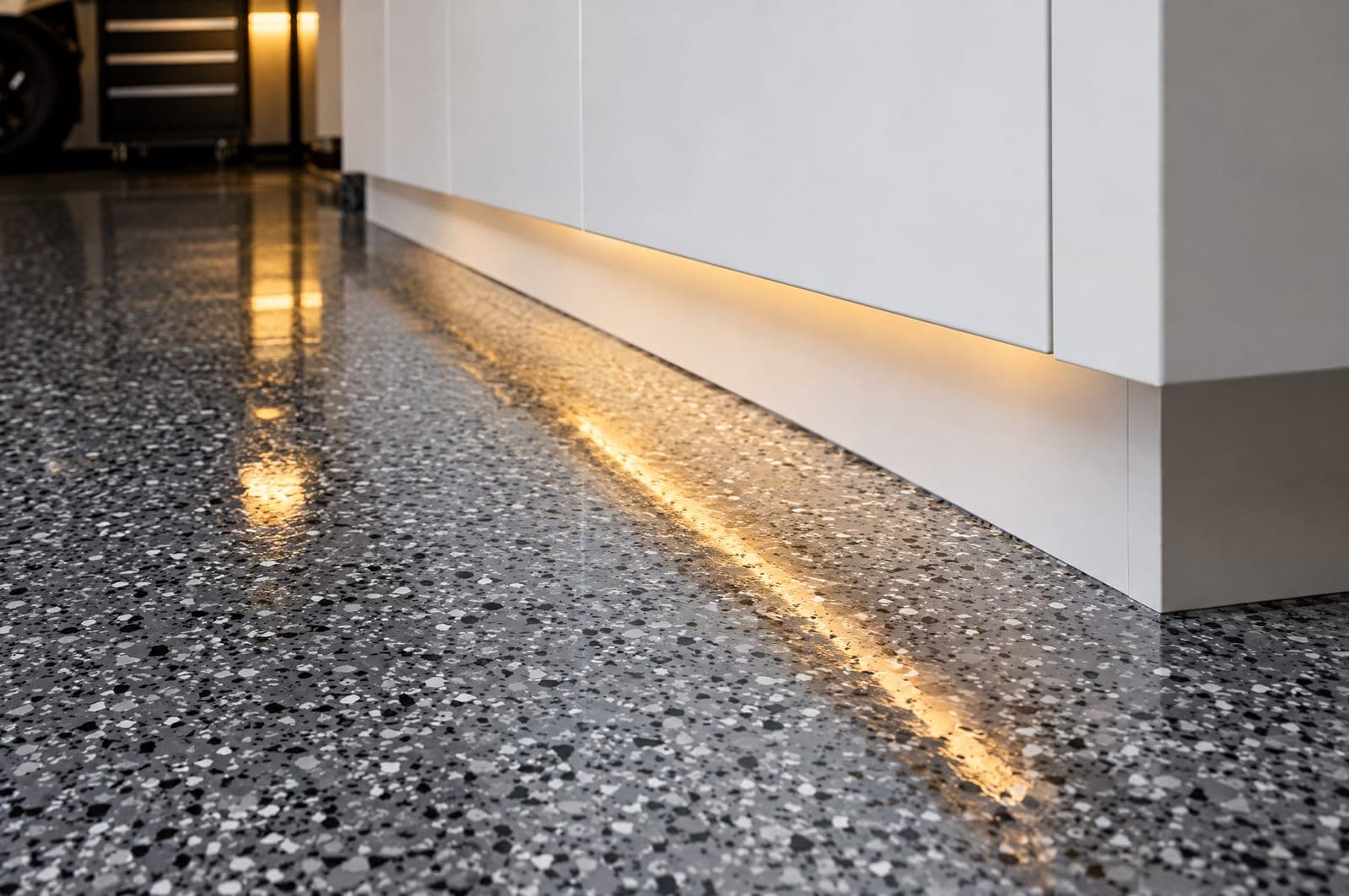 Gray flake epoxy garage floor meeting the base of a white cabinet with a warm light reflection